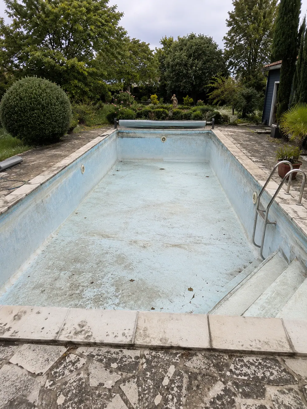 Bassin de piscine vidangé avec liner abîmé et finitions vieillissantes, avant rénovation par membrane armée